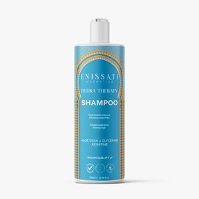 Une bouteille bleue de shampooing Hydra Therapy d'Enissati Cosmetics avec des accents dorés et blancs, contenant de l'aloe vera, de la glycérine et de la kératine, idéale pour une hydratation intense et parfaite pour maintenir le lissage brésilien.  Idéal pour ceux qui recherchent un lissage brésilien et explorent enissati avis. 
